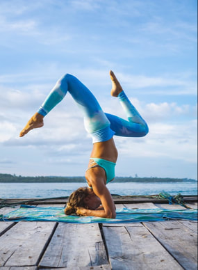ATHLETIC SURFER GIRL DOING YOGA AND PRACTICING HER HEADSTAND ON THE DOCK