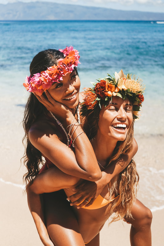 HAWAIIAN SURFER GIRL WEARING FLOWER CROWNS PLAYING TOGETHER ON THE SUNNY BEACH OF MAUI